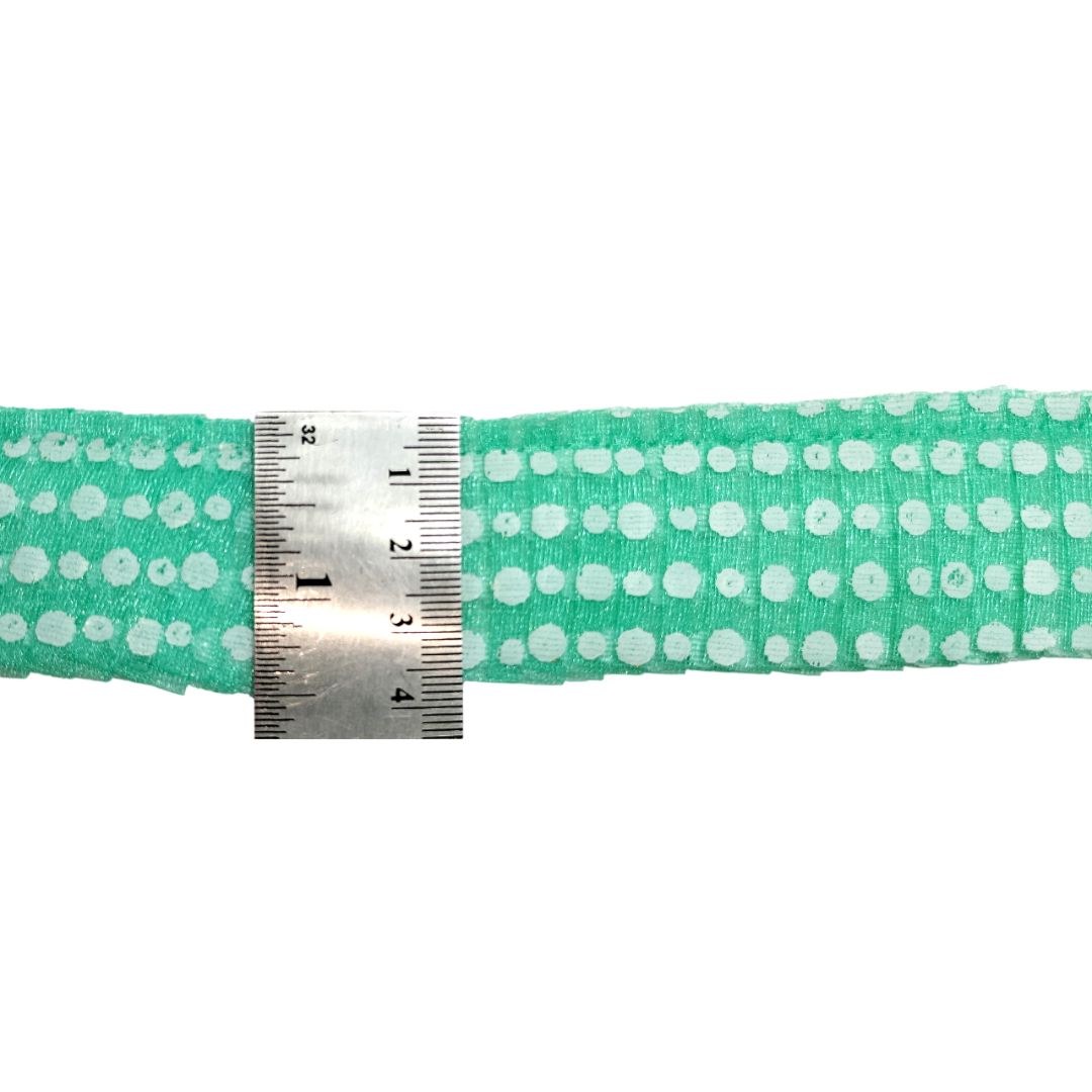 Green fabric with white polka dots and a metal ruler for scale on a white background