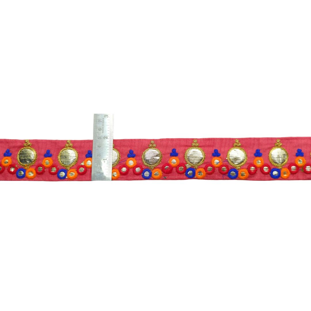 Decorative ribbon with colorful embellishments on a red background, measured against a ruler.