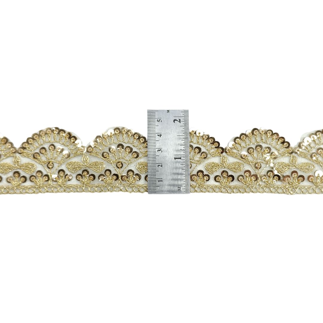 Decorative gold lace trim with a ruler for scale on a white background