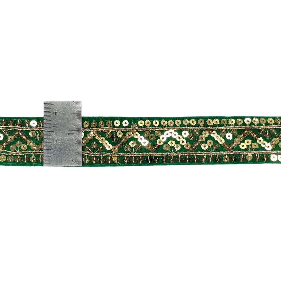Green ribbon with gold sequins and a ruler for scale on a white background