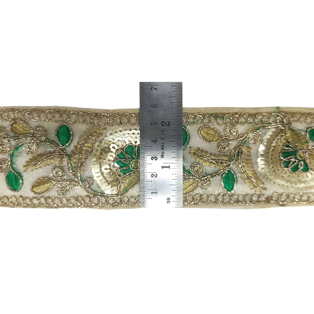 Decorative fabric trim with green and gold patterns, measured against a ruler on a white background.