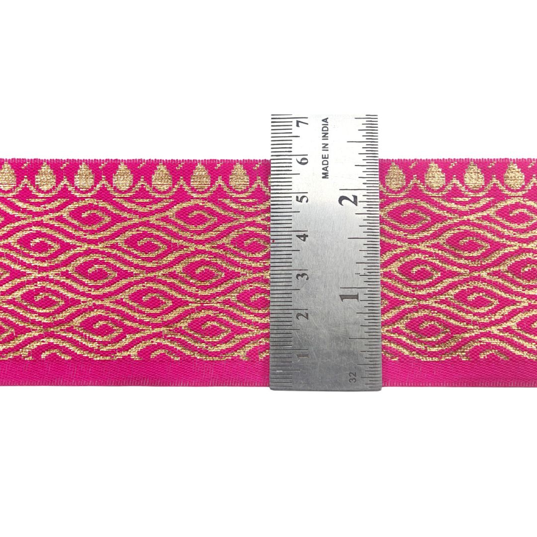 Pink ribbon with gold geometric pattern and a ruler for scale on a white background