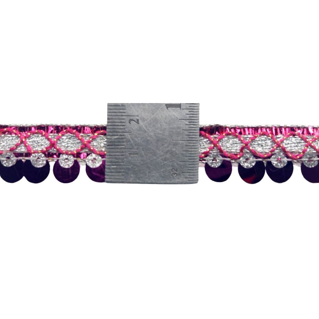 Close-up of a decorative trim with pink and purple pattern and silver accents, shown with a ruler for scale.