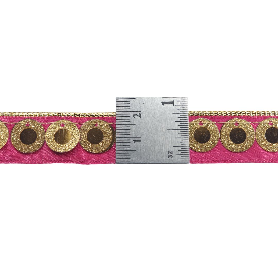 Pink ribbon with gold circular patterns and a ruler for scale on a white background