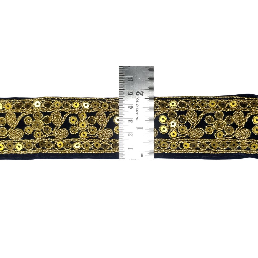 Black lace trim with gold embroidery and a ruler for scale on a white background