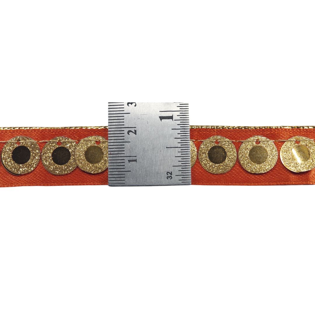 Orange ribbon with gold circular embellishments and a ruler for scale on a white background