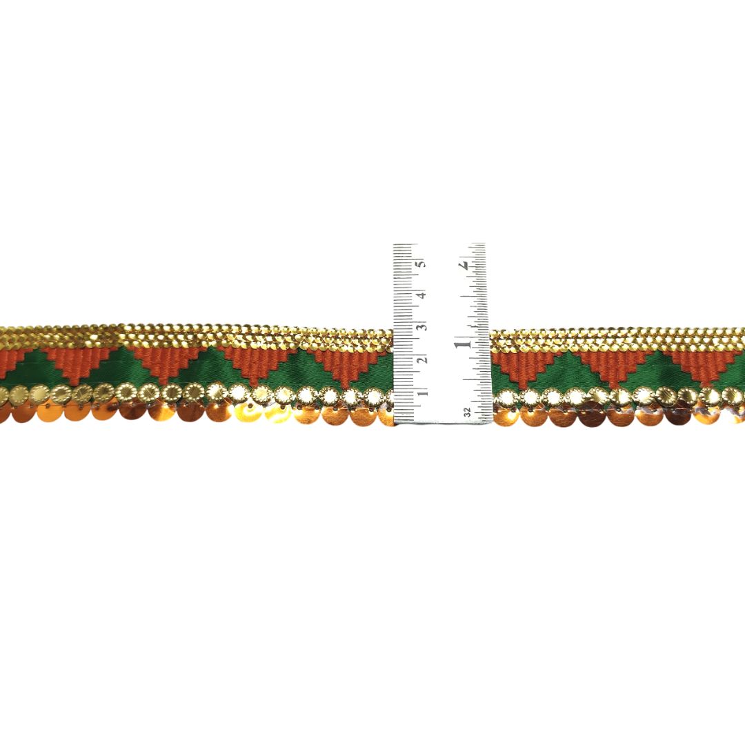 Decorative ribbon with gold, green, and red pattern next to a ruler on a white background