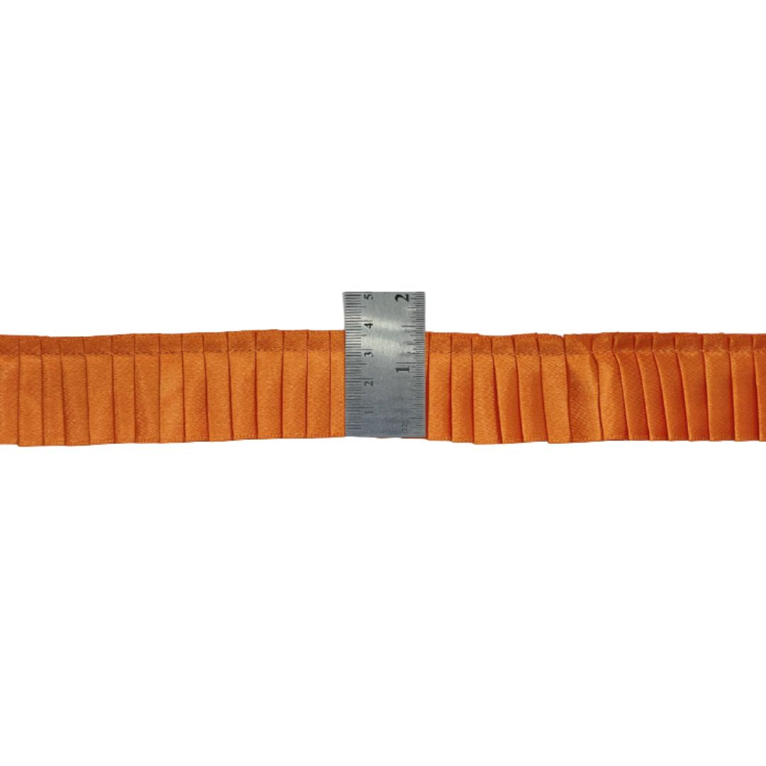 Orange pleated fabric with a metal ruler for scale on a white background