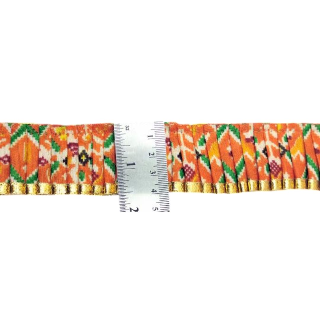 Decorative ribbon with a pattern of orange, green, and gold on a white background, with a ruler for scale.