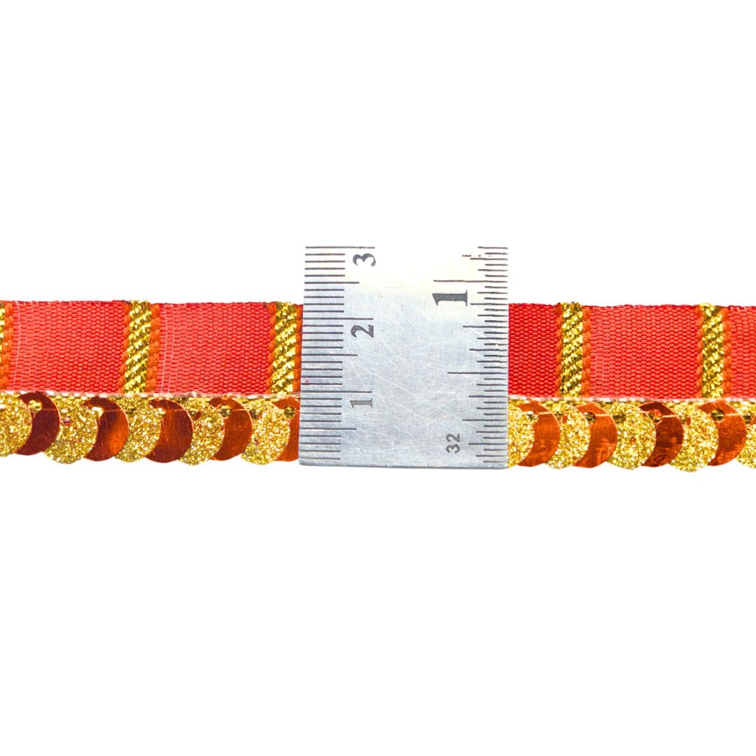 Red ribbon with gold decorative elements and a ruler for scale on a white background