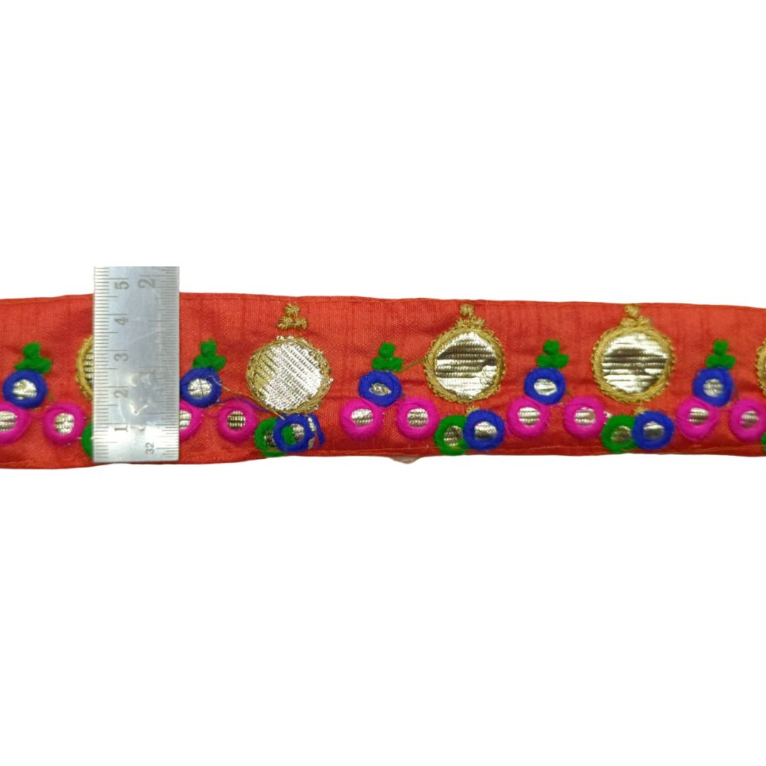 Decorative red band with colorful embellishments and a ruler for scale on a white background