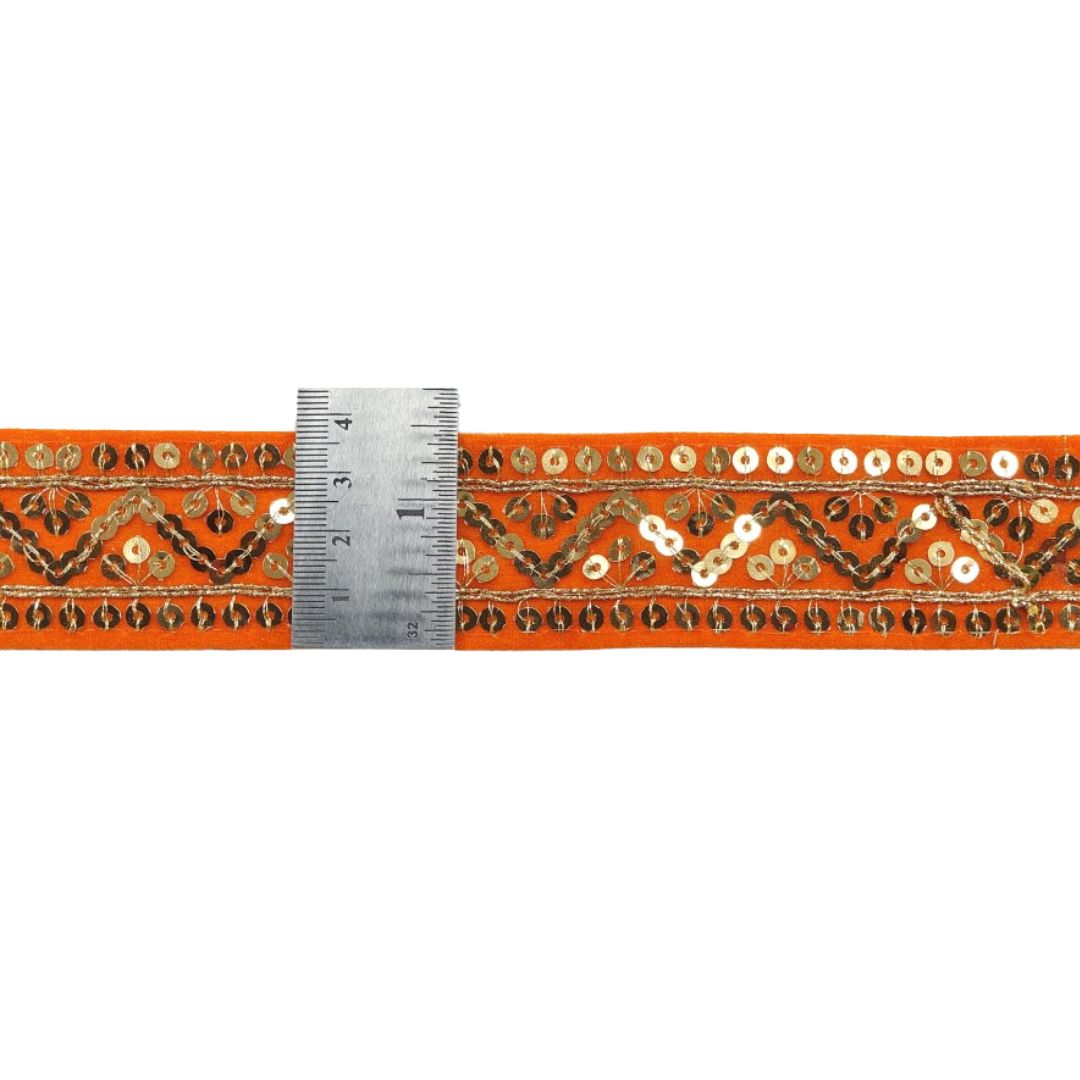 Decorative ribbon with gold and white patterns on an orange background, measured against a ruler.