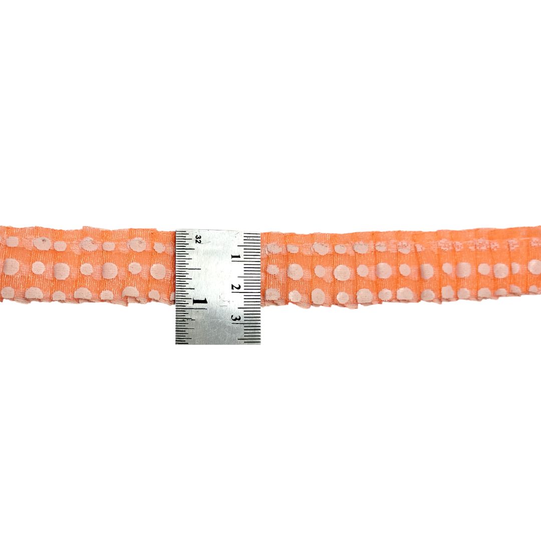 Orange belt with white polka dots and a metal ruler for scale on a white background