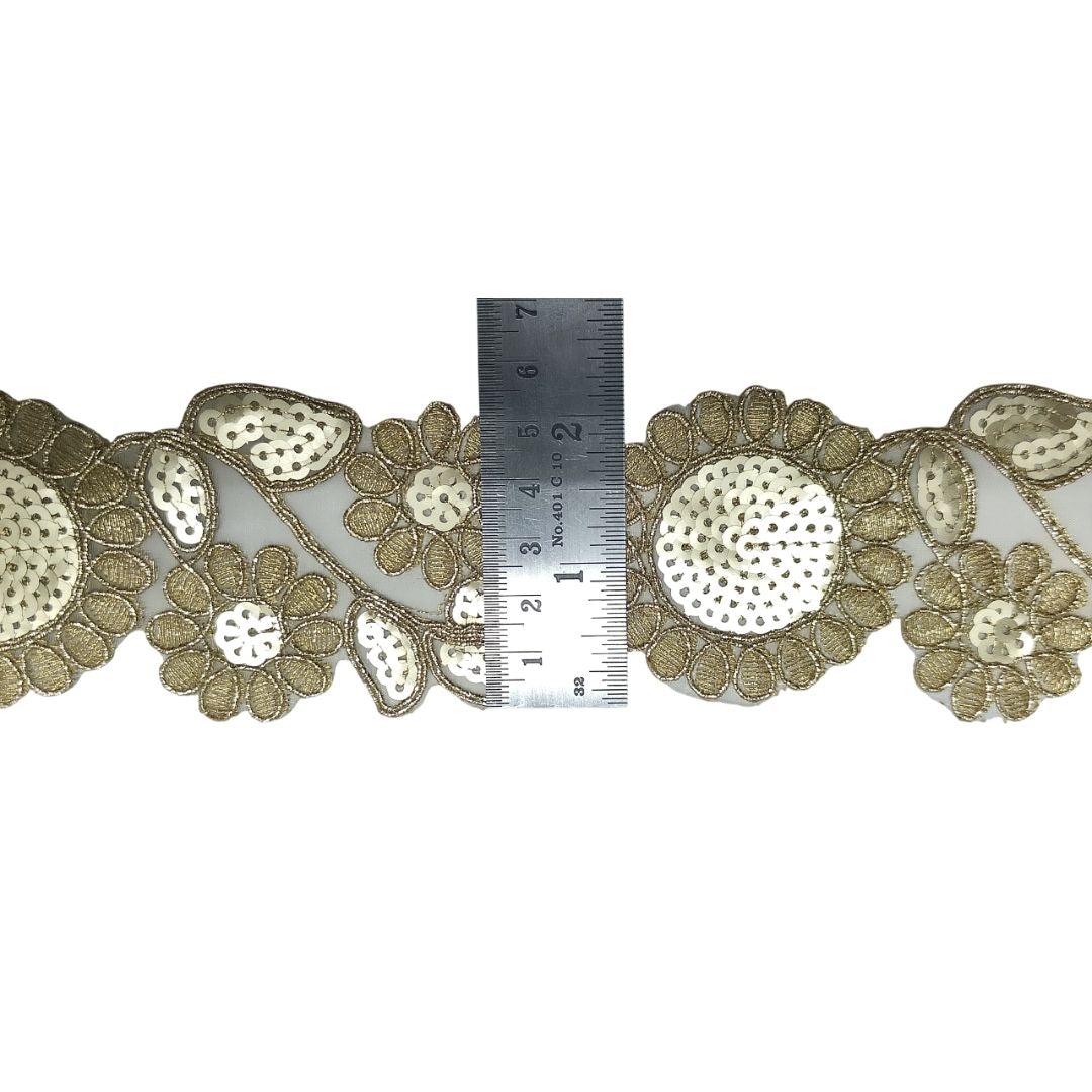 Decorative gold lace trim with a ruler for scale on a white background