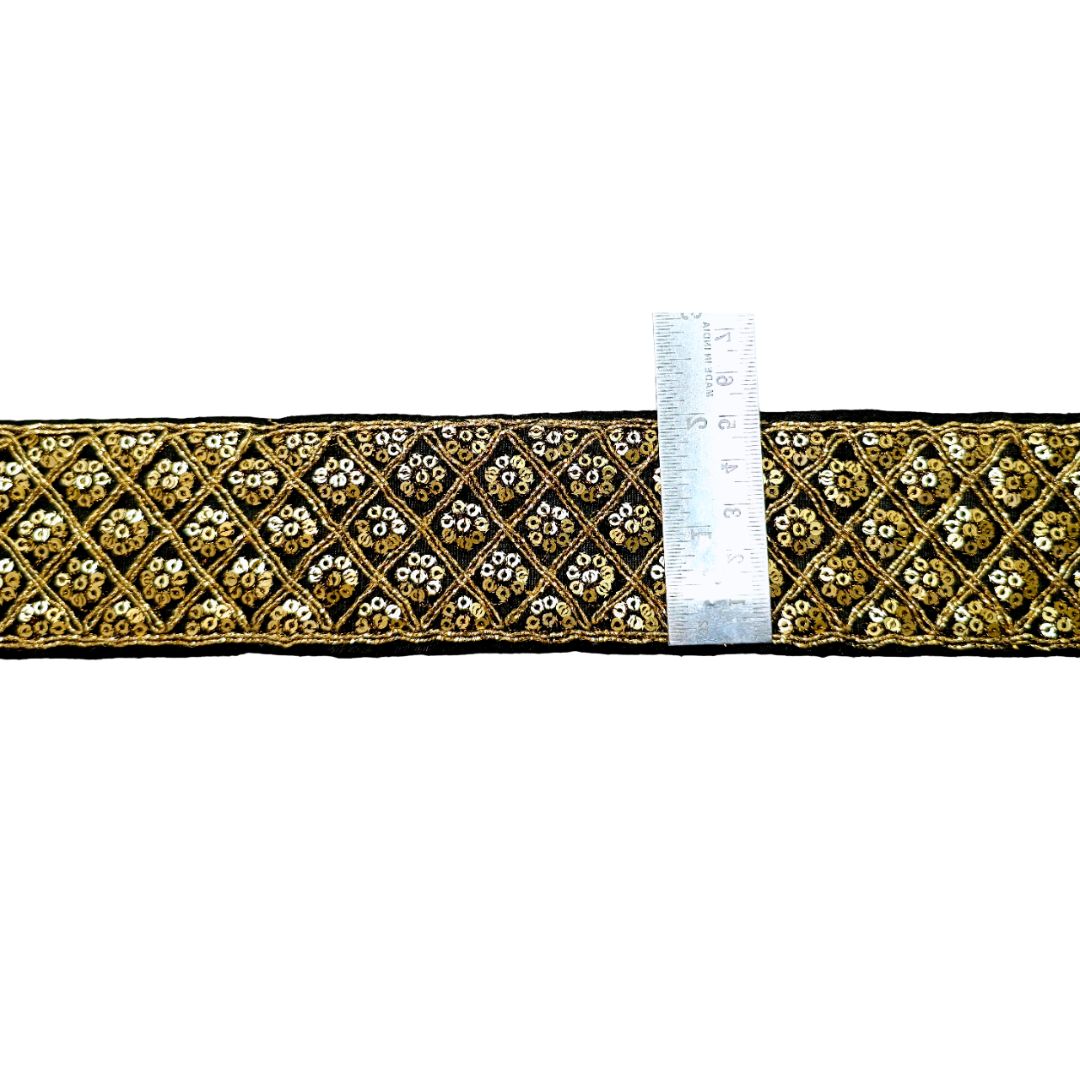 Decorative ribbon with gold and black pattern next to a ruler on a white background