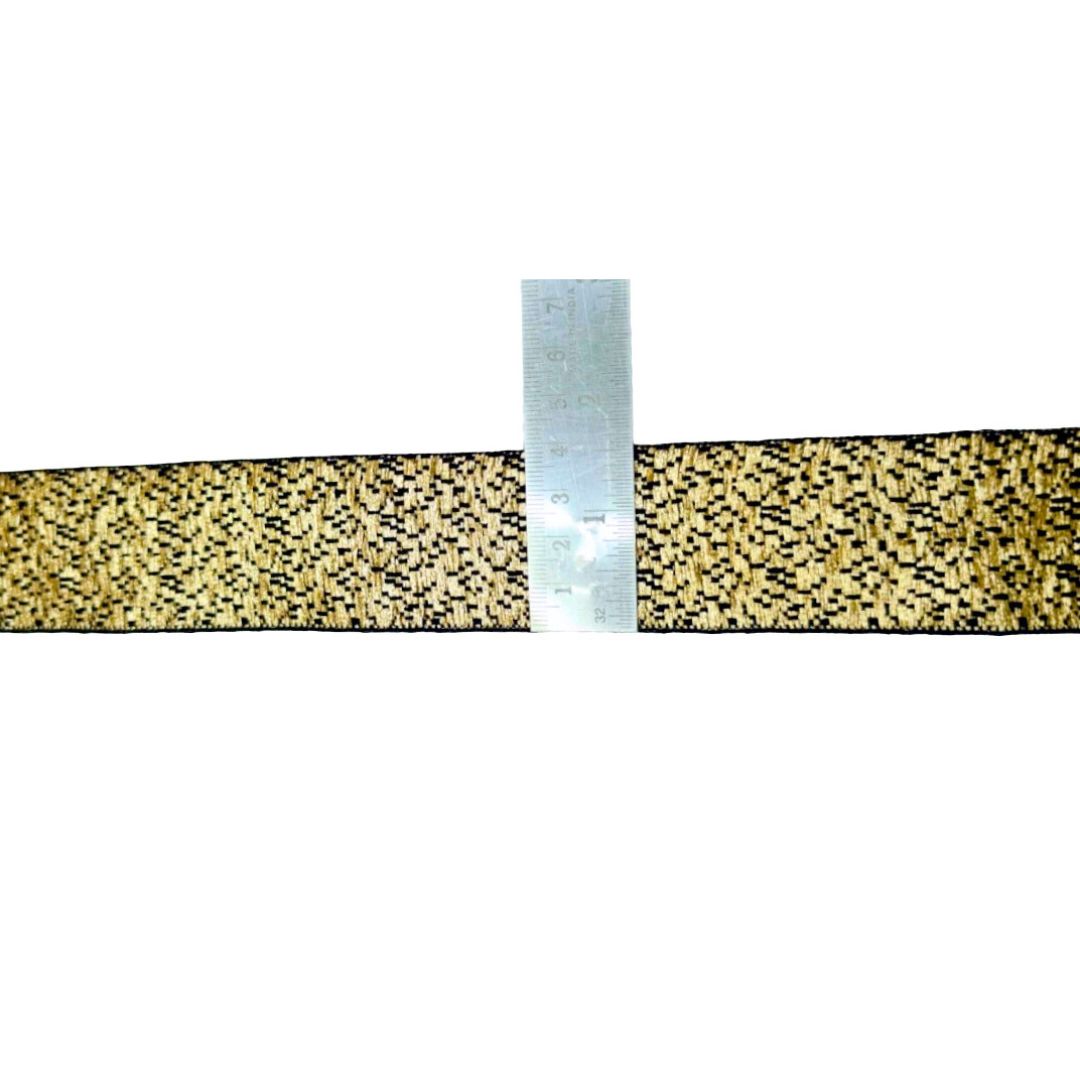 Gold and black patterned ribbon with a ruler for scale on a white background