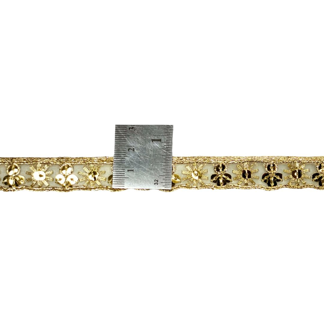 Decorative gold lace trim with a ruler for scale on a white background