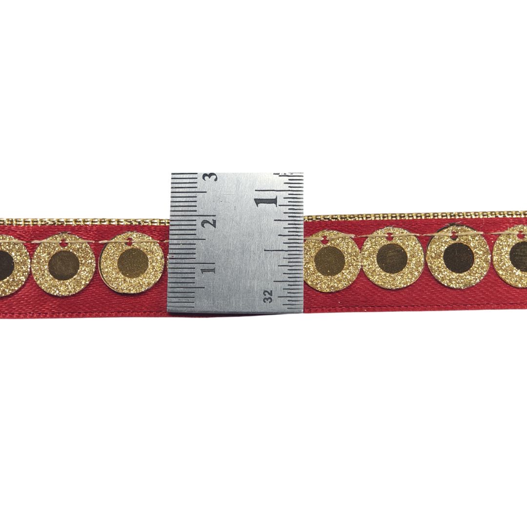 Red ribbon with gold circular patterns and a ruler for scale on a white background