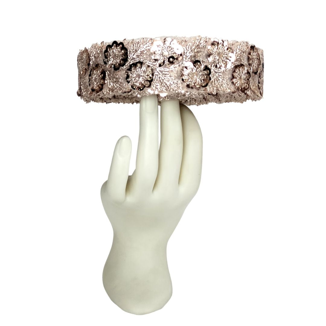 Decorative headband with floral patterns held by a white mannequin hand on a white background