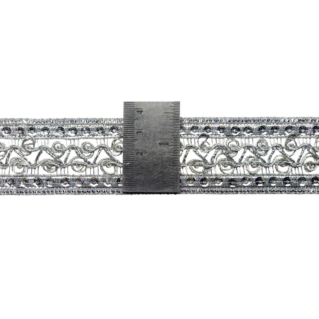 Decorative silver lace trim with a ruler for scale on a white background