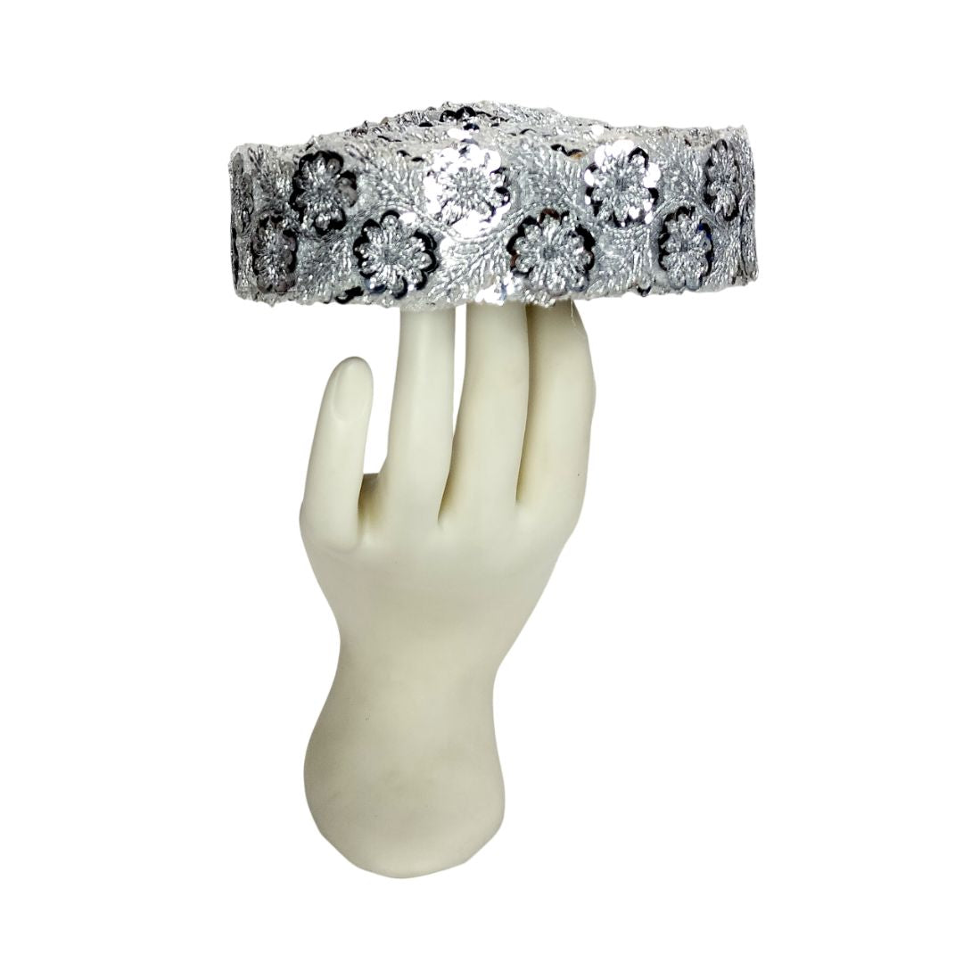 Silver headband with floral patterns on a mannequin hand against a white background