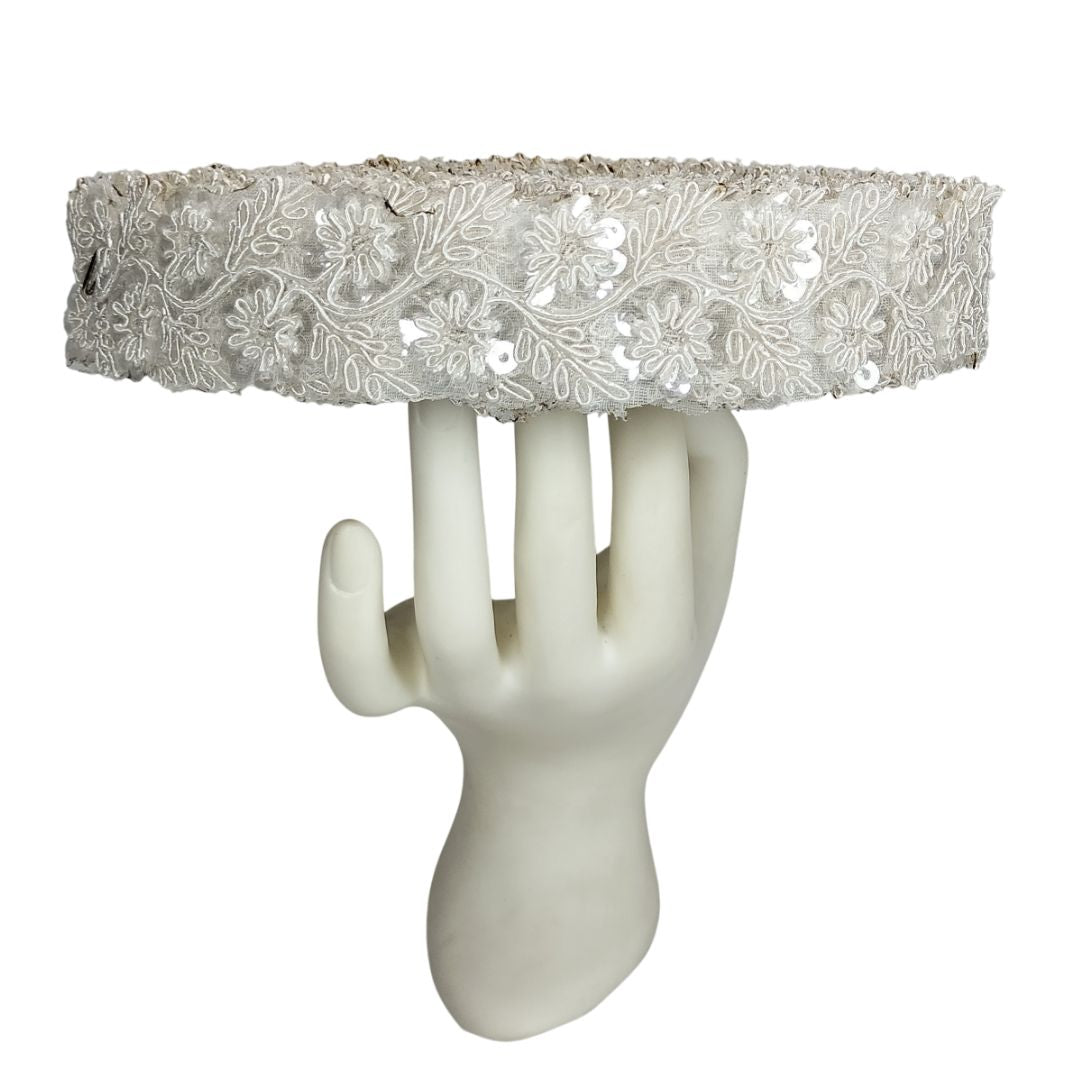 Decorative headband with floral lace design on a mannequin hand against a white background