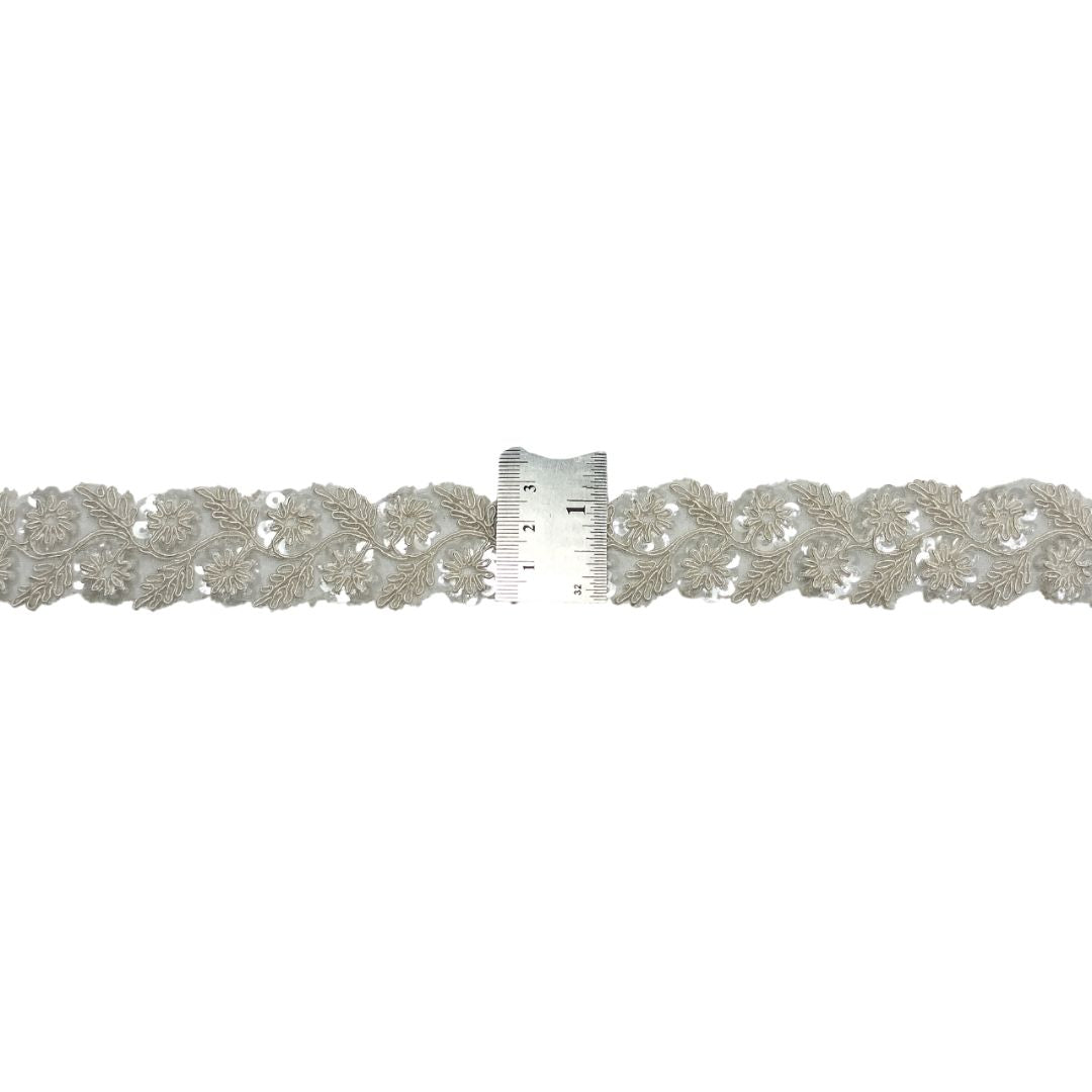 Silver lace trim with a ruler for scale on a white background