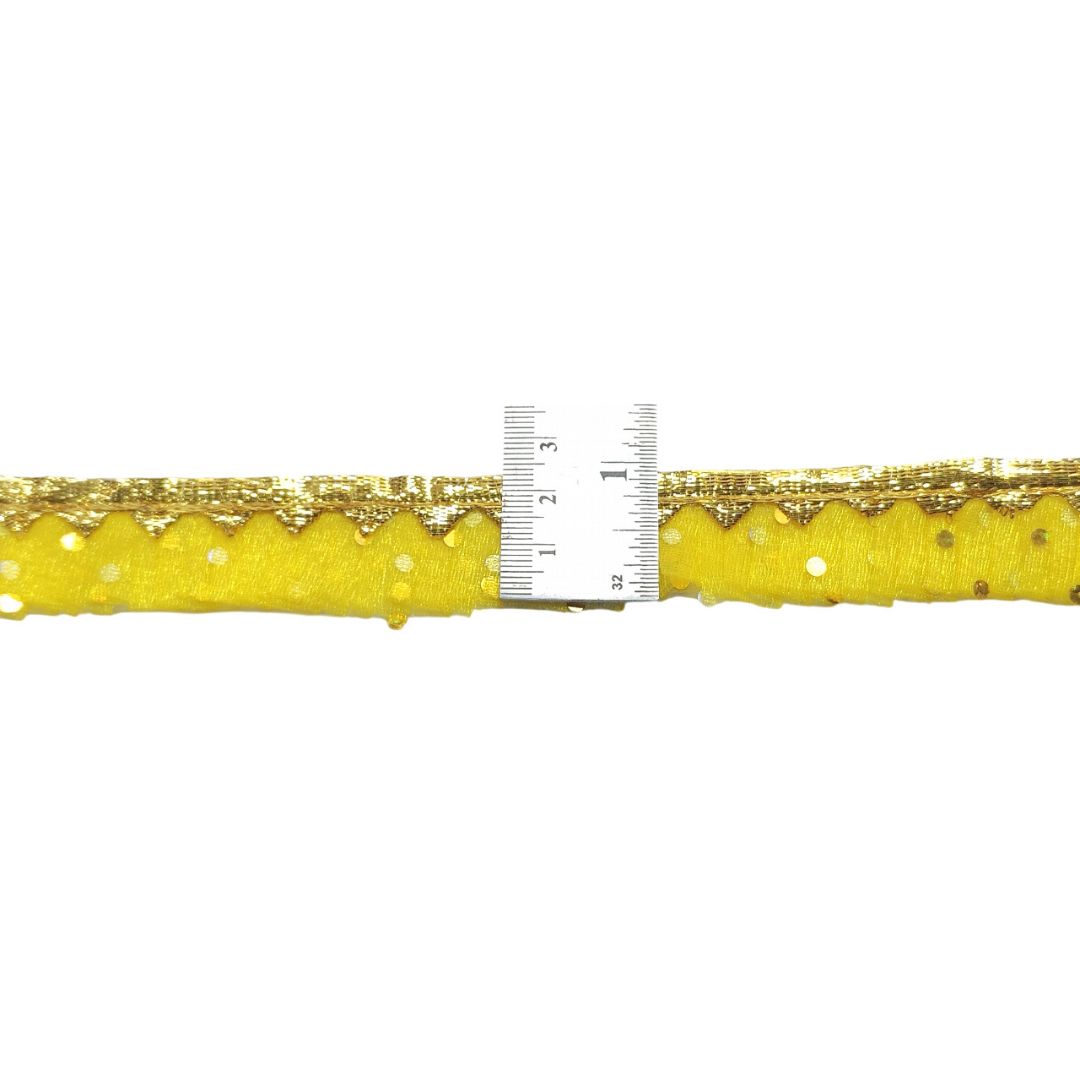 Close-up of yellow fabric with gold lace trim and a ruler for scale on a white background