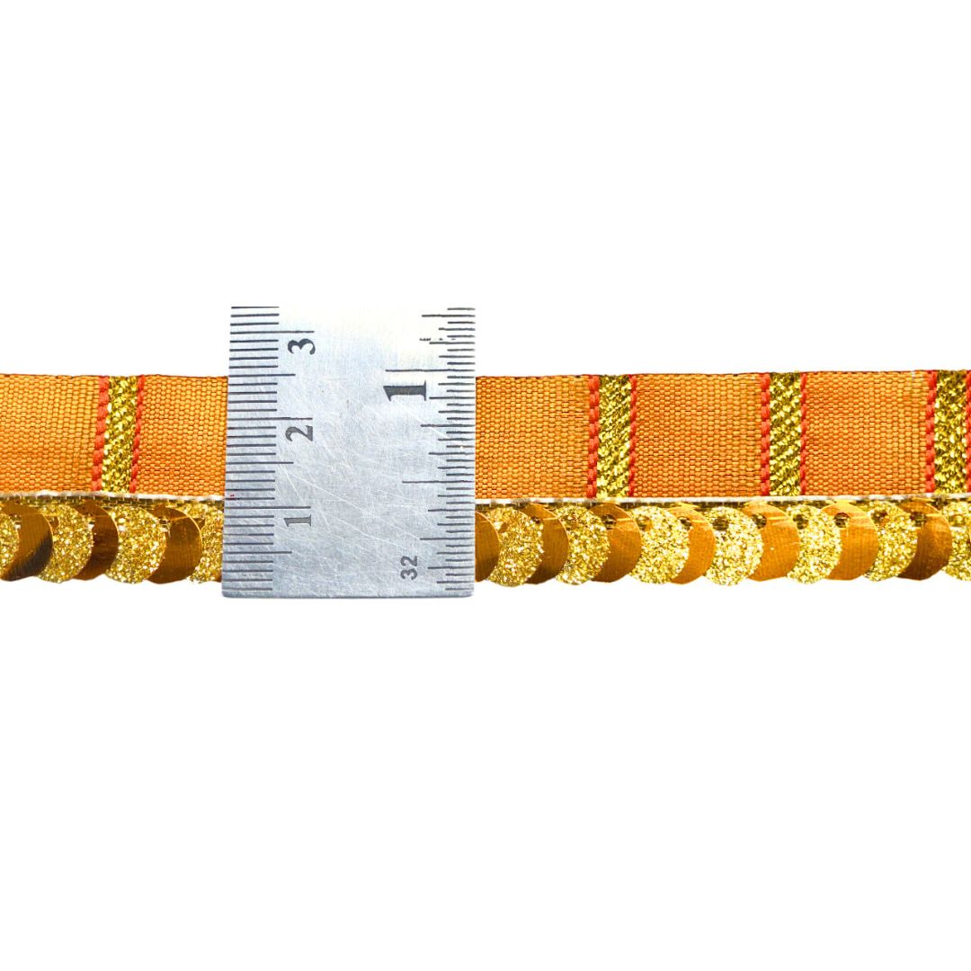 Orange ribbon with gold decorative elements and a ruler for scale on a white background