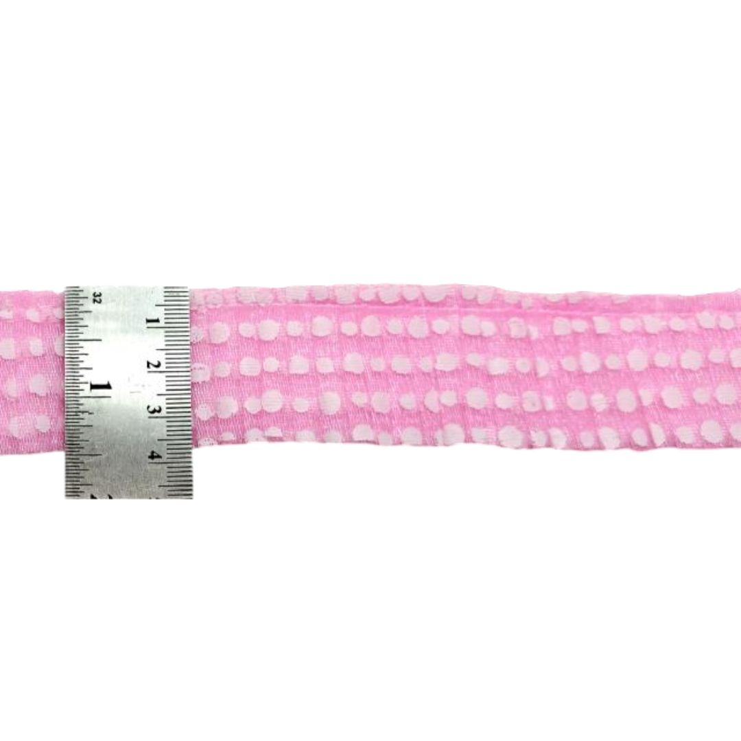 Pink fabric with white polka dots and a metal ruler for scale on a white background