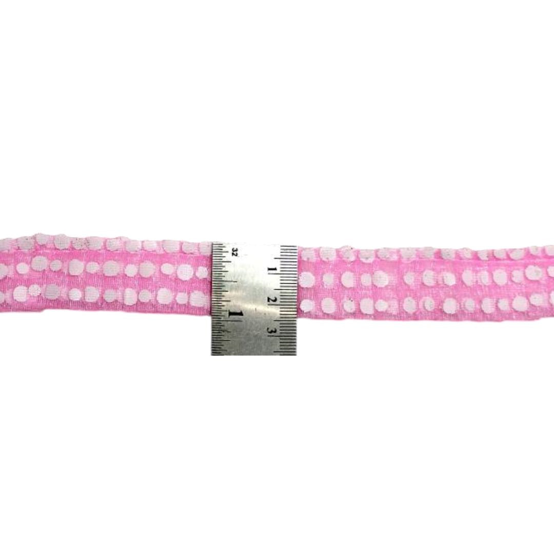 Pink fabric with white polka dots and a metal ruler for scale on a white background
